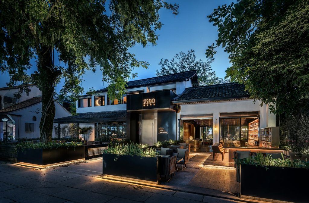 A modern restaurant with outdoor seating and a sign reading 2100 Club at dusk