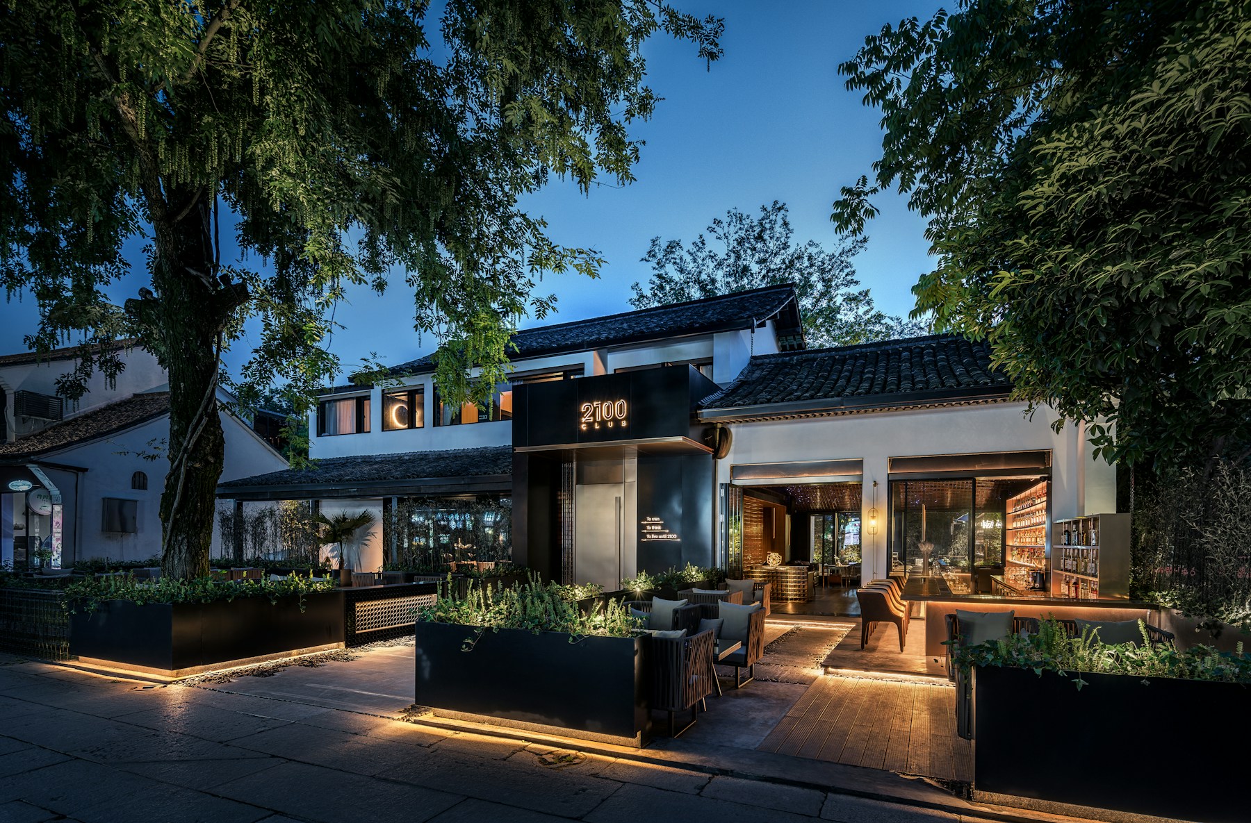 A modern restaurant with outdoor seating and a sign reading 2100 Club at dusk